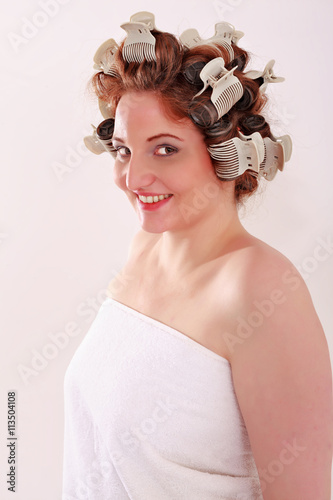 Portrait einer jungen vollbusigen Frau nur mit einem Handtuch bekleidet und Lockenwickler im Haar die in die Kamera lächelt