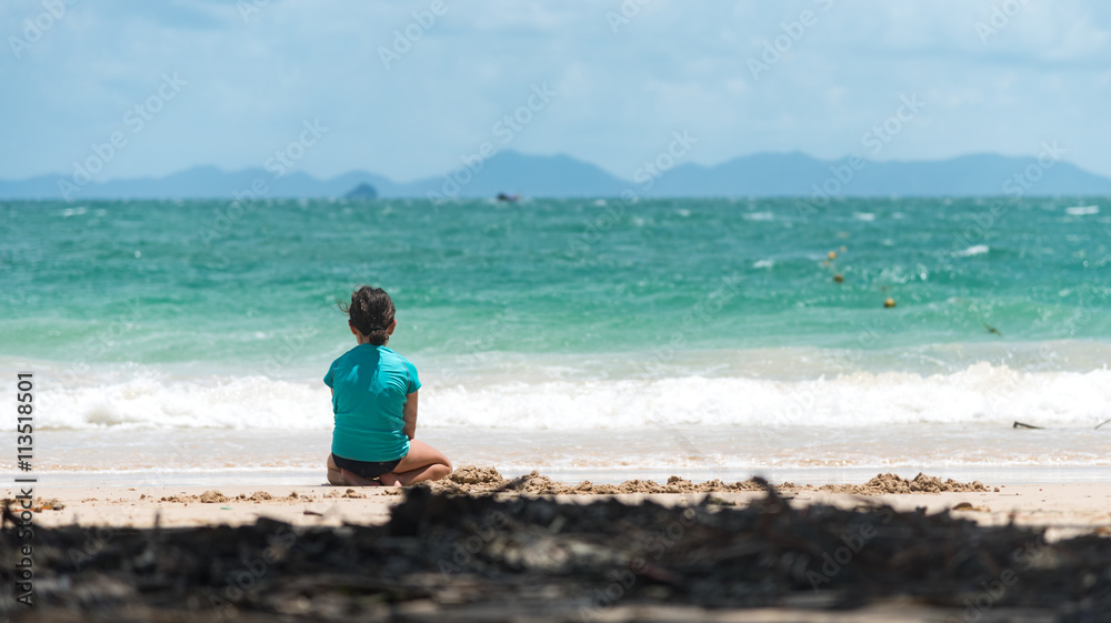 Girl sitting alone on sandy beach doing sand play