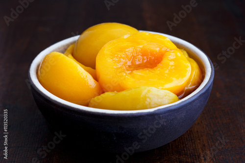 Canned peach halves in bowl isolated on dark background. In pers