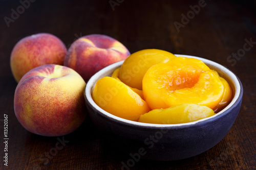 Fényképezés Canned peach halves in bowl on dark background with whole fresh