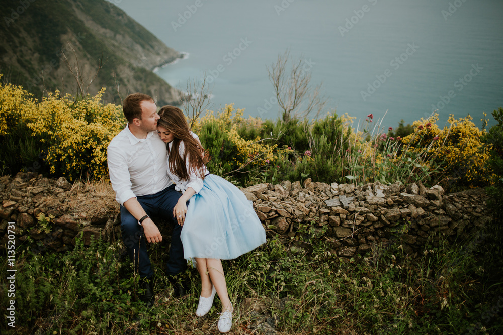 Young cute couple honeymoon sit on rocks posing and holding their hands on dating in a beautiful place italy near ocean and mountains, hug, smile and talk to each other
Young cute couple honeymoon sit on rocks posing and holding their hands on dating in a beautiful place italy near ocean and mountains, hug, smile and talk to each other
