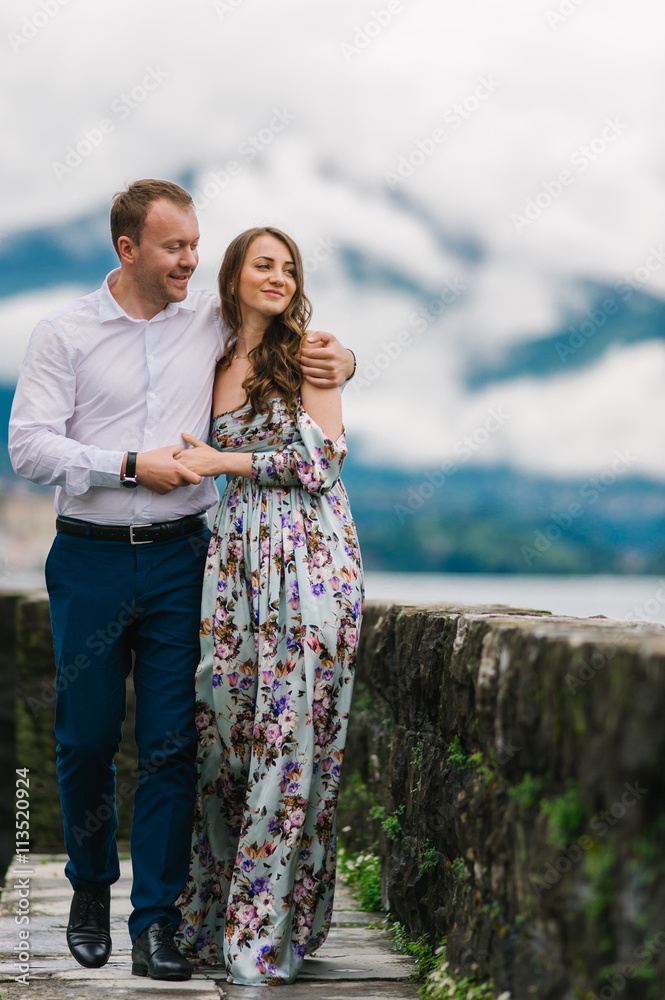 Young cute couple honeymoon walks holding their hands on dating in a beautiful place italy near ocean and mountains, hug, smile and talk to each other