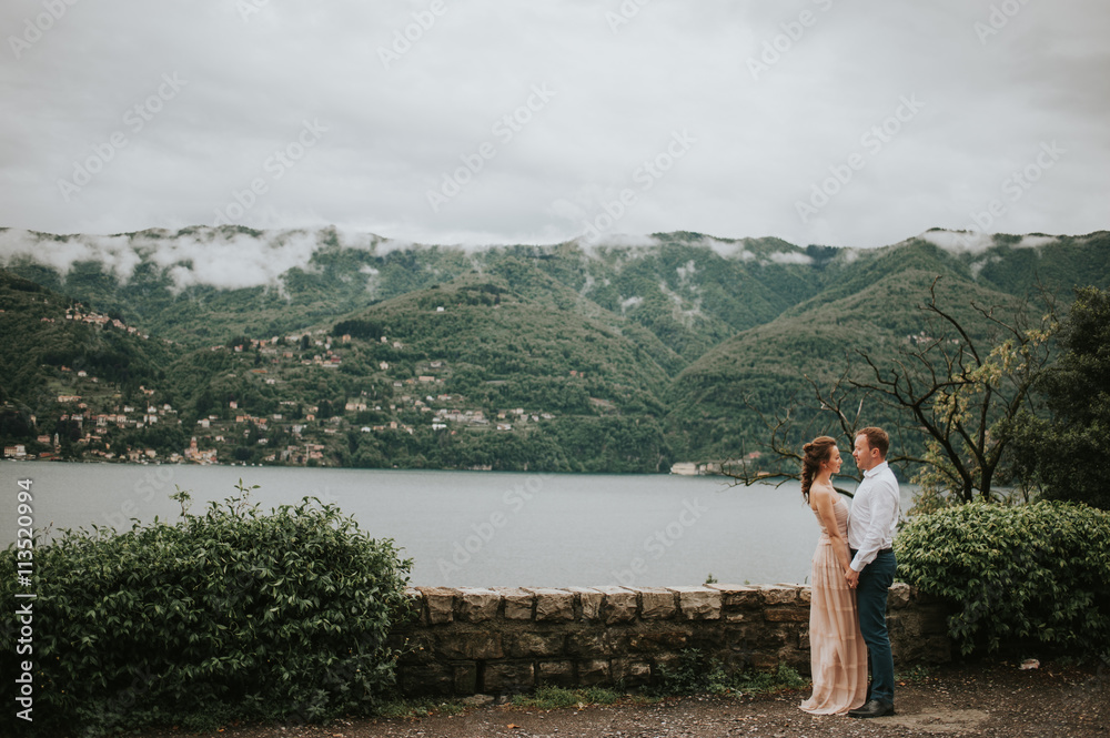 Fototapeta premium Young cute couple honeymoon walks holding their hands on dating in a beautiful place italy near ocean and mountains, hug, smile and talk to each other