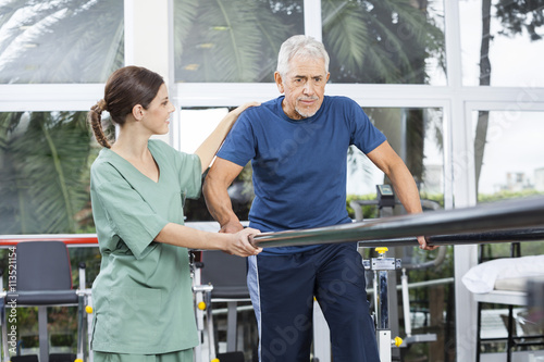 Female Physiotherapist Motivating Senior Patient To Walk Between