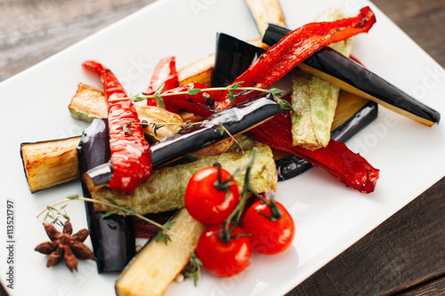 Grilled vegetables on white plate. Close-up of white plate with grilled vegetable strips. Grilled paprika, eggplant and vegetable marrow with cherry tomato on white plate top view.