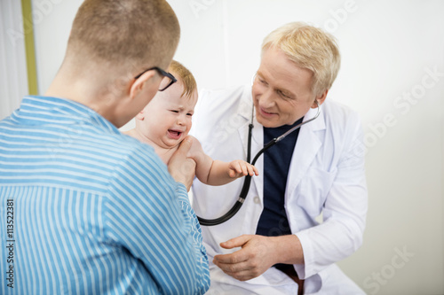Doctor Examining Crying Baby Held By Mother