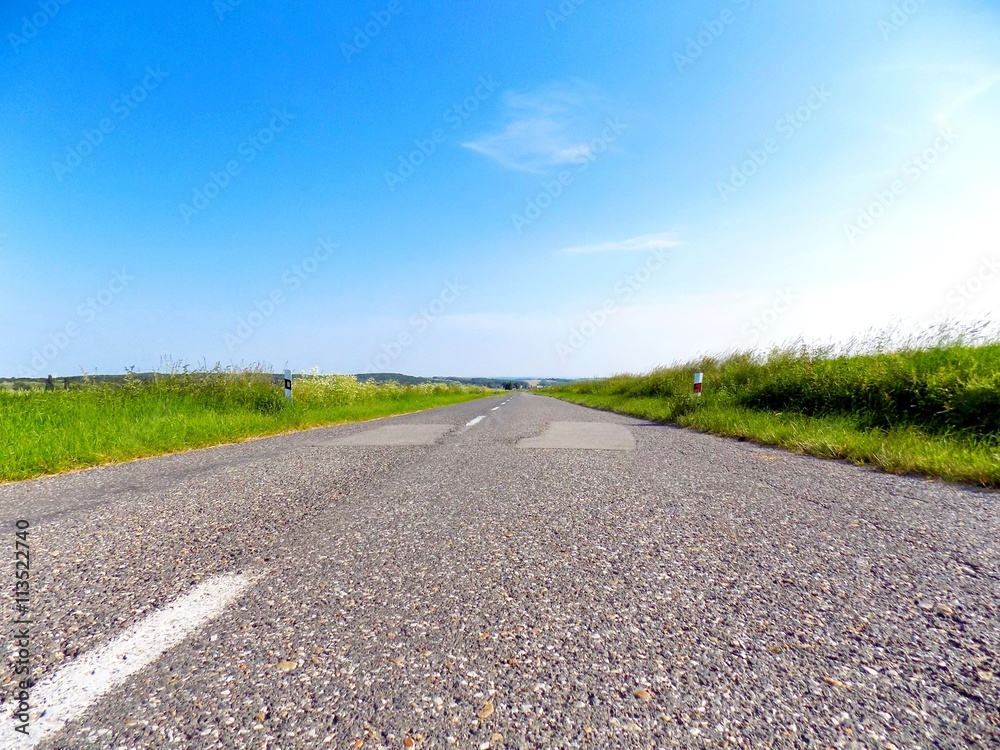 Asphalt road between fields during sunny day Asphalt road between fields during sunny day
