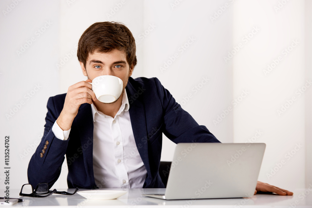 Young businessman sitting at the office desk and drinking Young businessman sitting at the office desk and drinking
