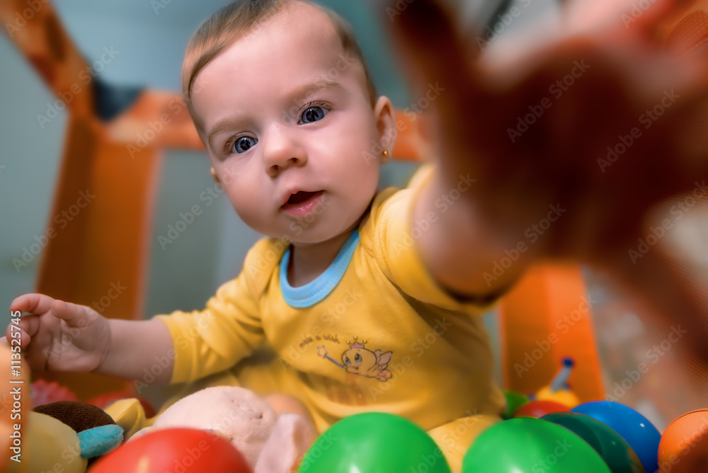 Obraz premium Beautiful baby lying among colorful balls reaching out for toys