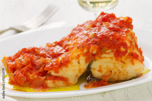 cod fish with tomato sauce on white dish and glass of white wine