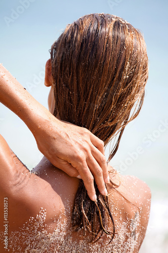 femme sur le sable qui touche ses cheveux mouillés