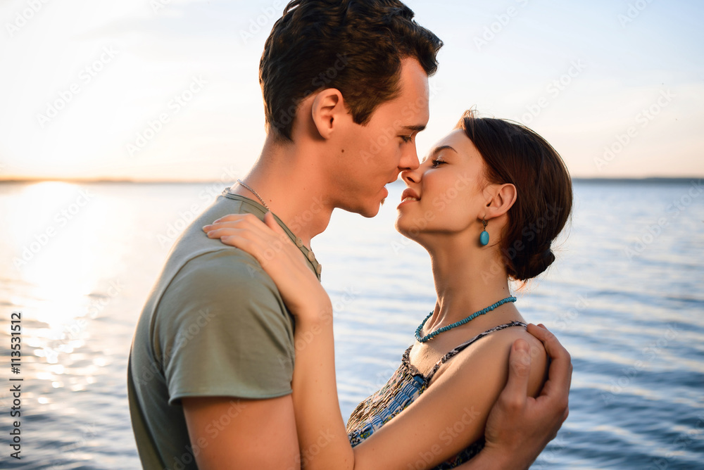 Happy beautiful couple walking and embracing on the beach of the sea at sunset Happy beautiful couple walking and embracing on the beach of the sea at sunset