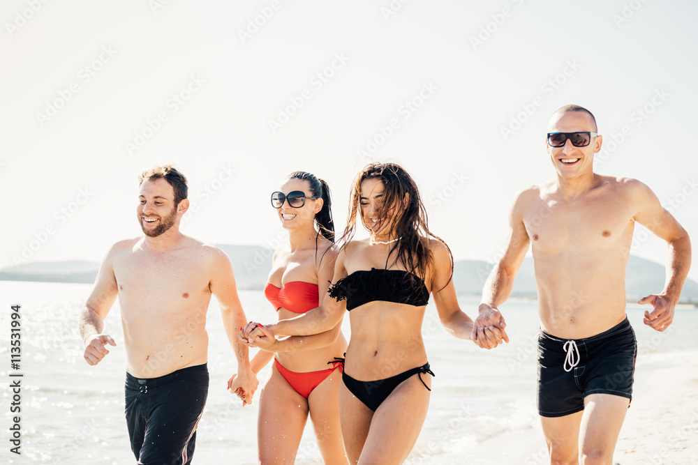 group of young multiethnic friends women and men at the beach in summertime running hand to hand smiling - friendship, happiness concept