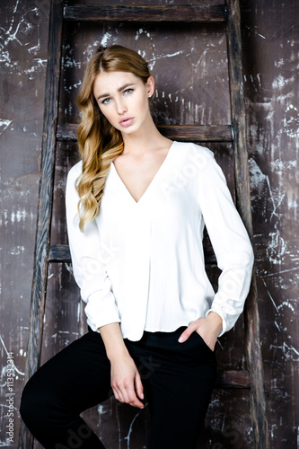 A young slim woman wearing white blouse posing in the room.