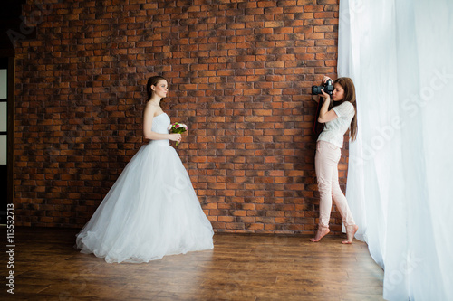 Young sexy woman photographer is taking pictures the bride in the studio