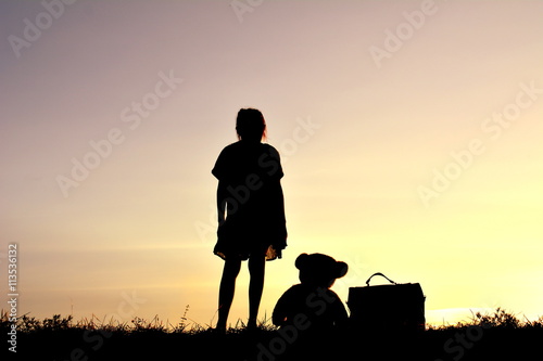 Silhouette a girl and bag with teddy bear at sky sunset
