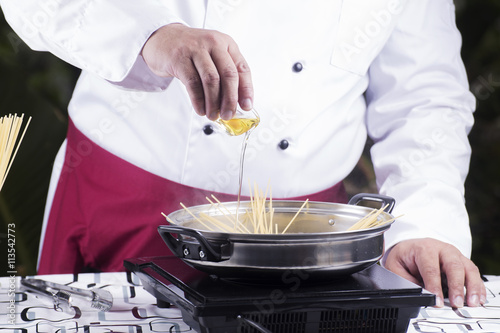 Chef pouring olive oil to spaghetti boiled in the pan