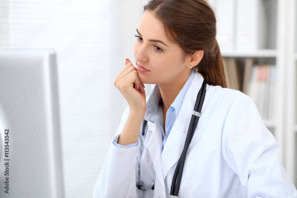 Young brunette female doctor sitting at the table and working at hospital office. Doctor is in trouble with diagnosis. Health care, insurance and help concept. Young brunette female doctor sitting at the table and working at hospital office. Doctor is in trouble with diagnosis. Health care, insurance and help concept.