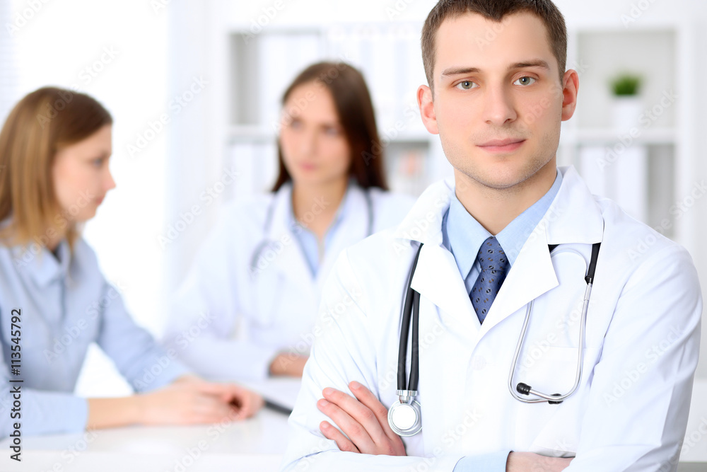 Friendly male doctor on the background with patient and his doctor in hospital. High level and quality medical service concept. Friendly male doctor on the background with patient and his doctor in hospital. High level and quality medical service concept.