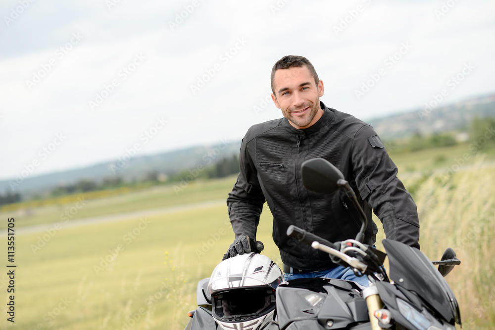 Naklejka premium przystojny młody człowiek rowerzysta z białym kaskiem, jazda na czarnym motocyklu