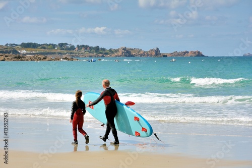 Père et fille marchent sur une plage de Bretagne où ils viennent de pratiquer le surf photo