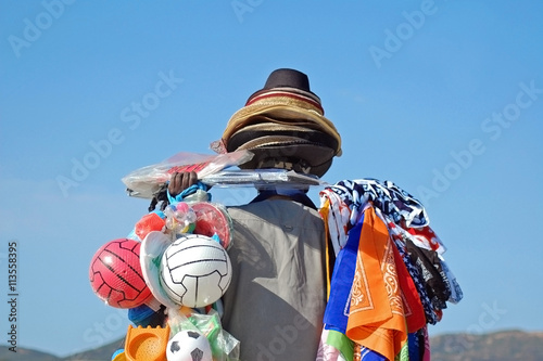 Beach hawker carrying lots of colorful balls, hats and scarves