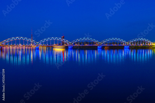 Illuminated railway bridge and reflection in Daugava river at tw