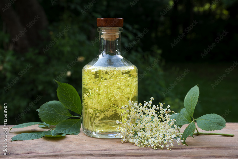 Homemade elderflower drink in a glass bottle on a wooden table in the garden
