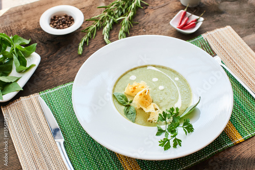 Soup puree zucchini, chicken broth and Parmesan crisp in a white plate on a wooden table © amixstudio