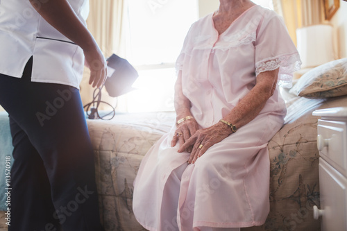 Home caregiver with senior woman sitting on bed