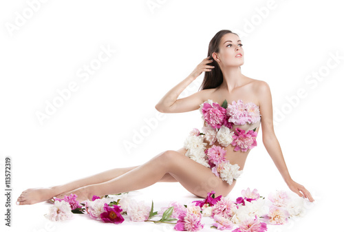 Young beautiful woman with flowers peonies. A girl sits on the floor with flowers. Flowers cover the body.