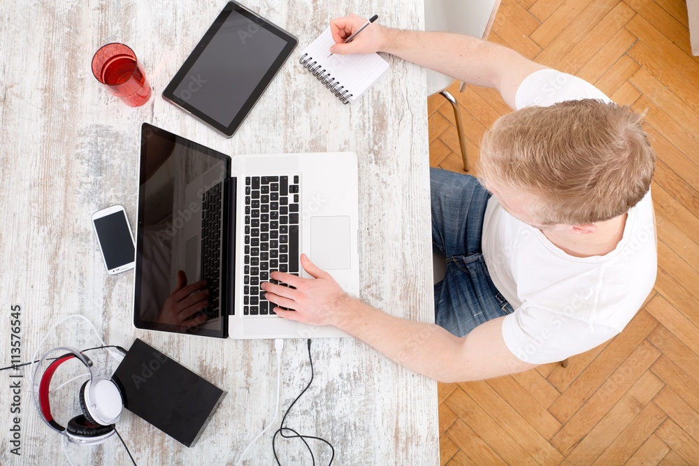 A young caucasian man working in his home office seen from above.. A young caucasian man working in his home office seen from above..
