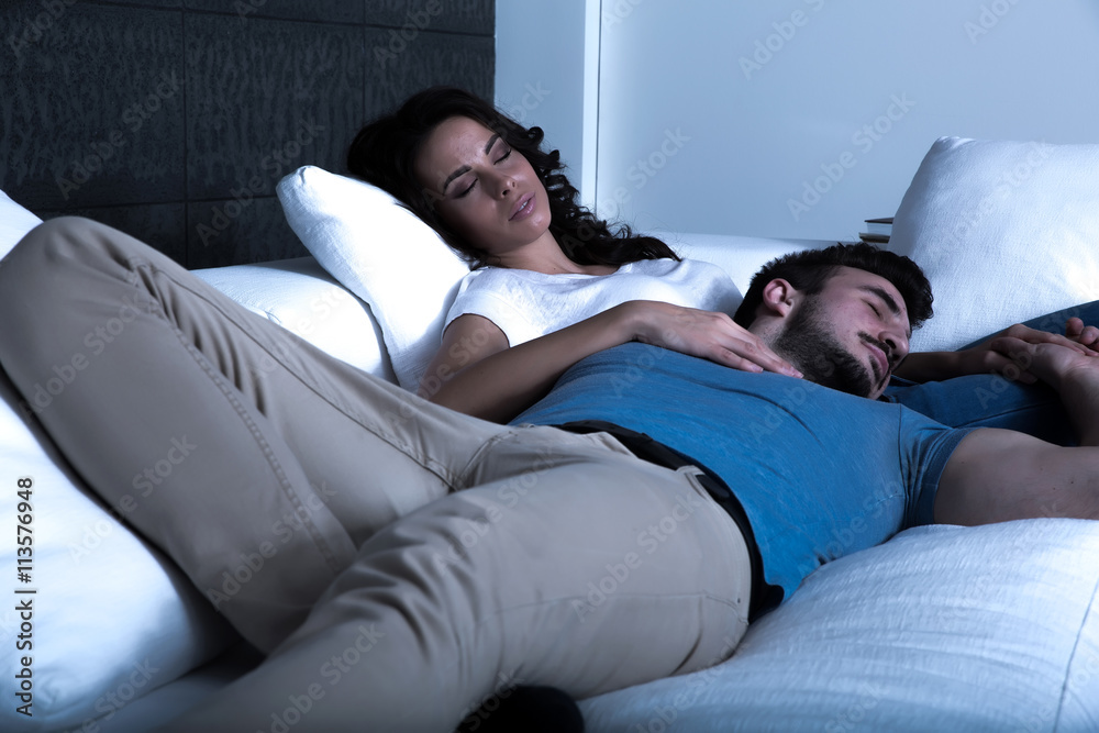 Young couple sleeping on the sofa at night. - obrazy, fototapety, plakaty 