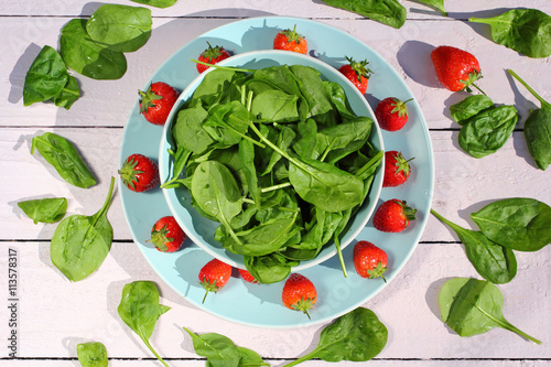 Fresh spinach salad with spinach and strawberries on wooden light pink table