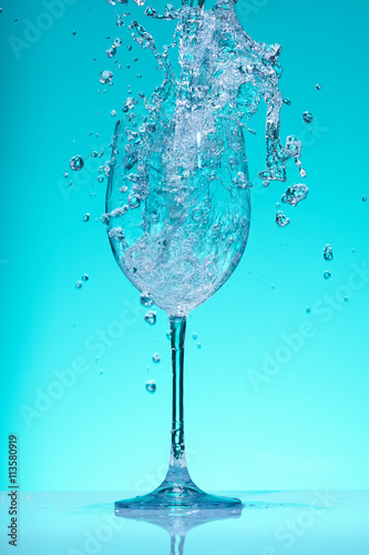 Water pouring into a big size wineglass with splashes.