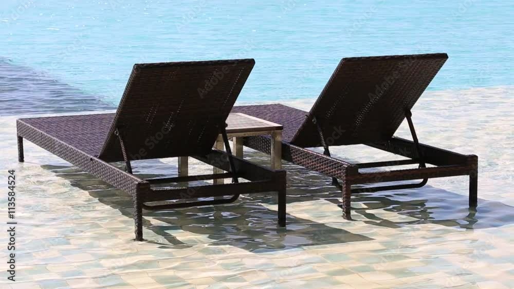 Two deck chairs in the swimming pool at a tropical resort Two deck chairs in the swimming pool at a tropical resort