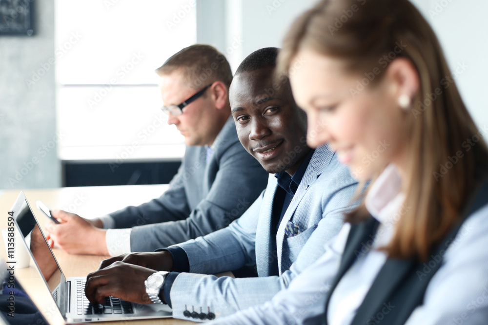 Portrait of smiling African American business man with executives working in background Portrait of smiling African American business man with executives working in background