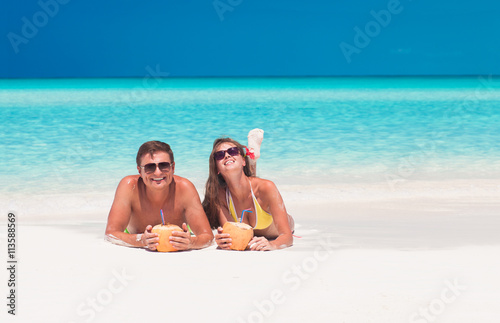 Photography happy young couple lying on a tropical beach in Cayo Largo and drinking a coconu