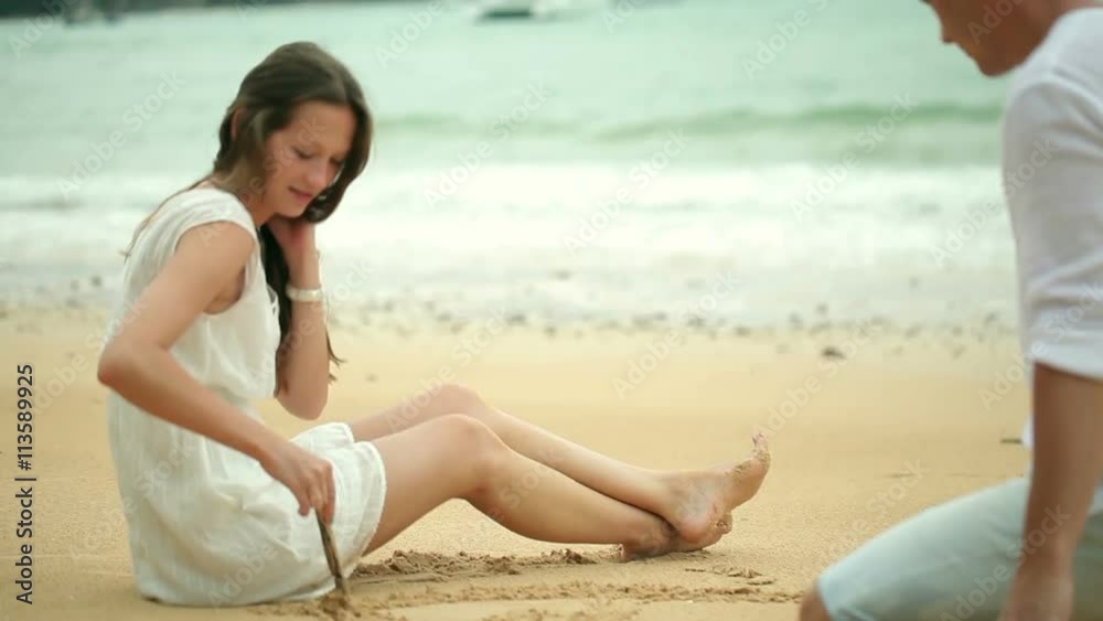 Romantic young couple draw heart shapes in the sand on the beach. Romantic young couple draw heart shapes in the sand on the beach.