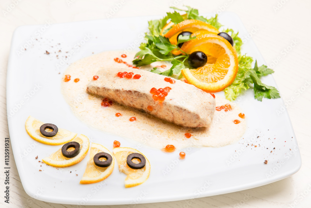 A piece of salmon with garnish and white sauce