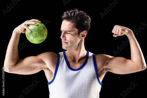 Confident athletic man holding ball and showing muscles