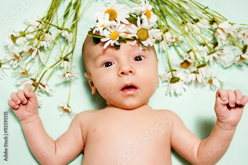 newborn baby lying on a green background with a bouquet of daisi photo