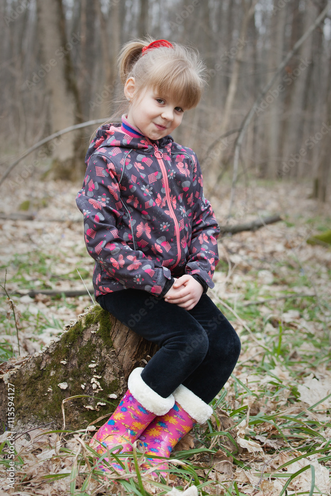 Fototapeta premium Portrait of a smiling young girl sitting on a stump in the spring forest