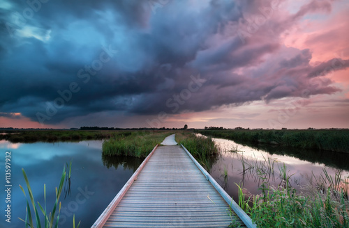 wooden path bridge over river at stormy sunset