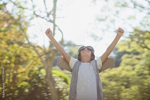 Excited boy standing in park with arms raised