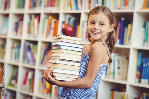 School girl holding stack of books in library