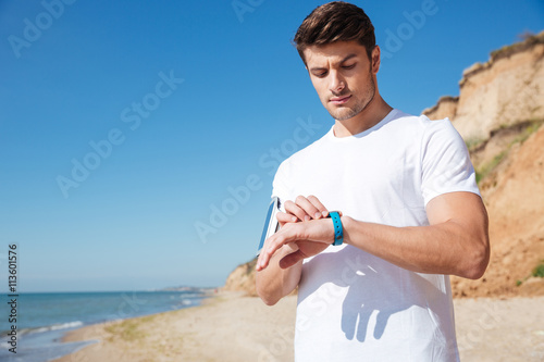 Sportsman standing and using smart watch on the beach