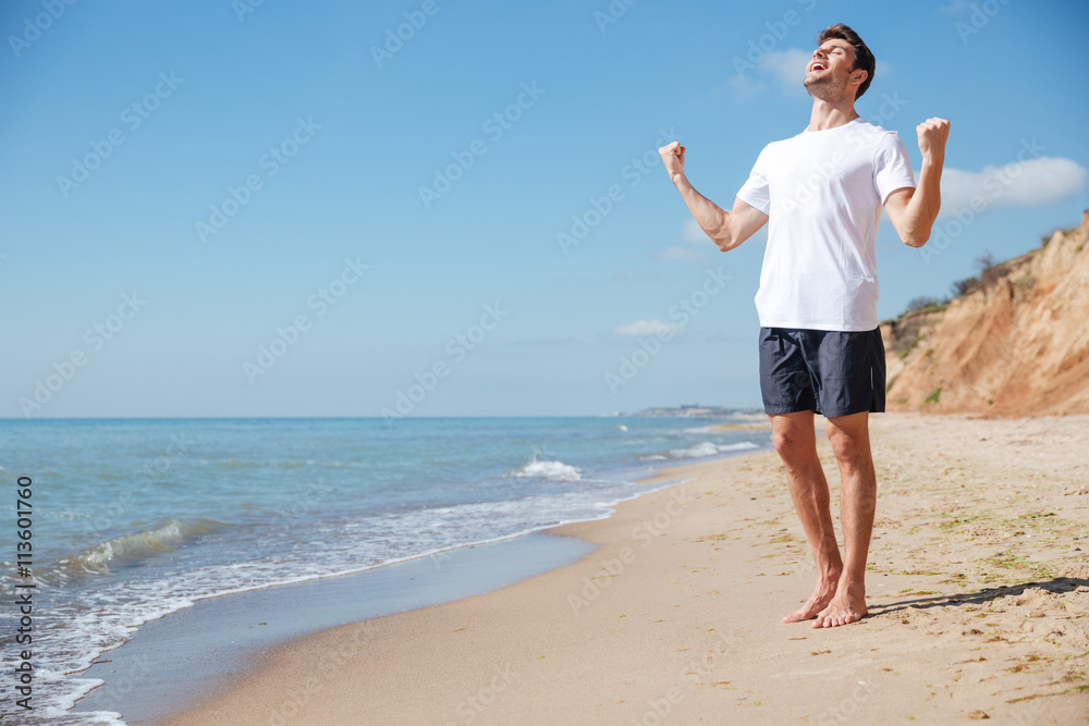 Happy excited man with raised hands celebrating success on beach Happy excited man with raised hands celebrating success on beach