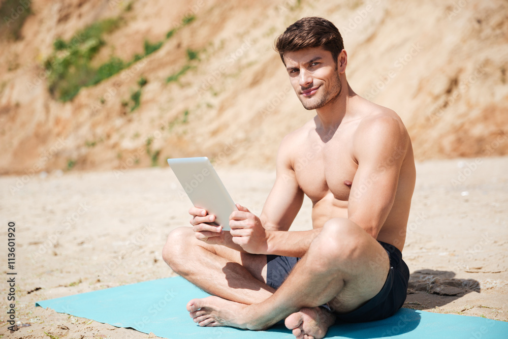 Smiling man sitting and using tablet on the beach