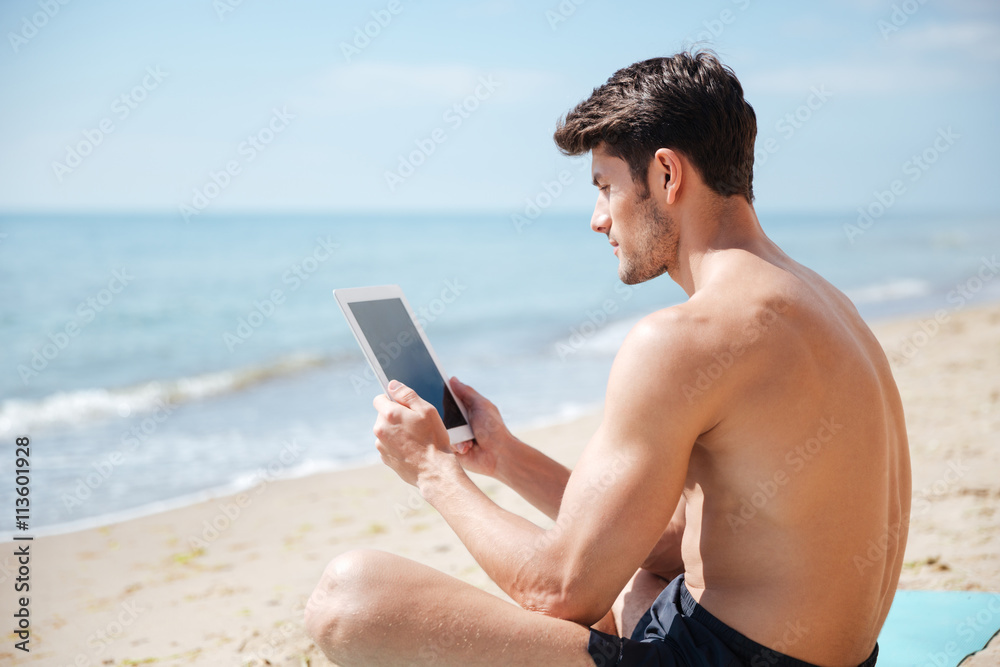 Handsome man using blank screen tablet on the beach